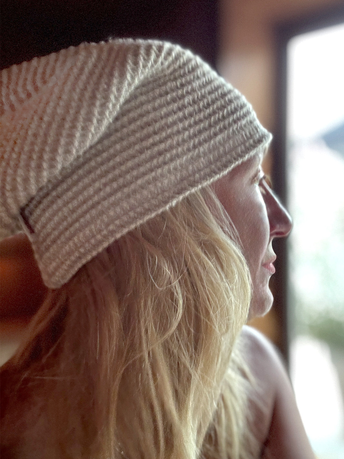 Eine blonde Frau hat eine Sauna-Muetze aus beigem Waffelpique-Stoff auf dem Kopf in der Sauna