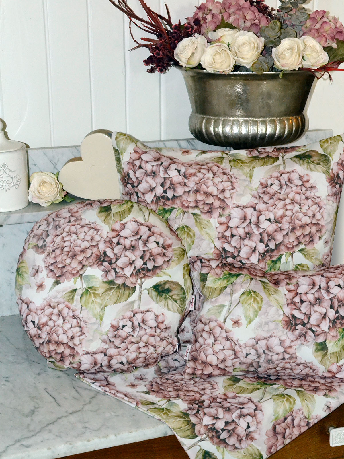 Drei Kissen bezogen mit je einem Kissenbezug im Landhausstil, bedruckt mit rosa/pinken Hortensien. Dekoriert auf einer Marmorplatte.