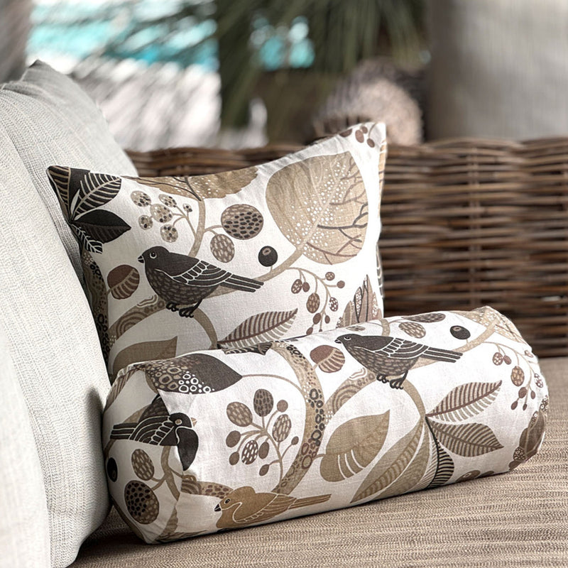 Dekorative Kissen mit Vogel- und Blättermuster in Naturtönen auf einem Sofa.