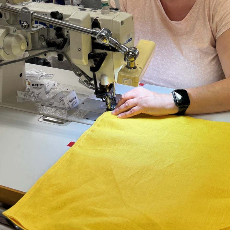 Eine Näherin näht mit einer Industrienähmaschine gelben Stoff. 