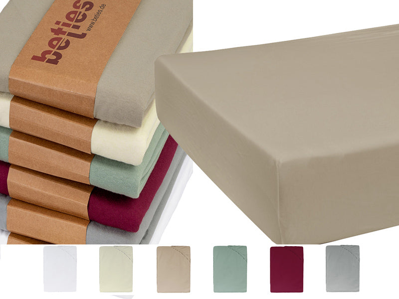 Ausschnitt einer beigen Matratze auf einem weissen Hintergrund. Daneben ein Stapel mit gefalteten Kissenbezuegen in den Uni-Farben Wei�, Hellgrau, Weinrot, Gruen, Natur und Beige.