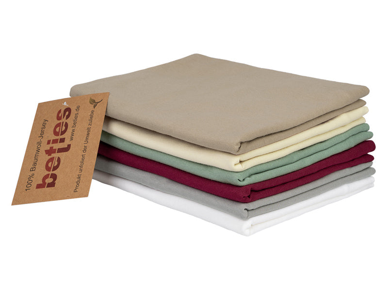 Stapel mit gefalteten Kissenbezuegen in den Uni-Farben Weiss, Hellgrau, Weinrot, Gruen, Natur und Beige.