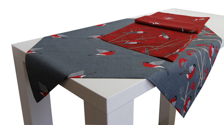 Graue und rote Mitteldecke auf einem weissen Tisch. Das Motiv auf der Tischwaesche, fliegende und sitzende rot-grau-schwarze Voegel auf Zweigen mit roten Beeren.