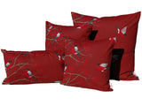 Drei quadratische und ein rechteckiges rotes Kissen in verschiedenen Groessen auf einem weissen Hintergrund. Die Kissenbezuege sind bedruckt mit rot-grau-schwarzen Voegeln die auf Zweigen mit roten Beeren sitzen oder teilweise fliegen.