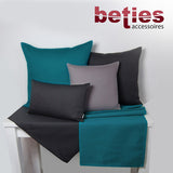 Hellbeige und Weinrote Tischwaesche auf einem weissen Tisch. Darauf stehen vier Kissen mit einfarbigen Kissenbezuegen in den Farben Hellbeige, Dunkelgrau und Weinrot.