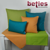 Gelbe und Apfelgruene Tischwaesche auf einem weissen Tisch. Darauf stehen vier Kissen mit einfarbigen Kissenbezuegen in den Farben Petrol, Gelb und Gruen.