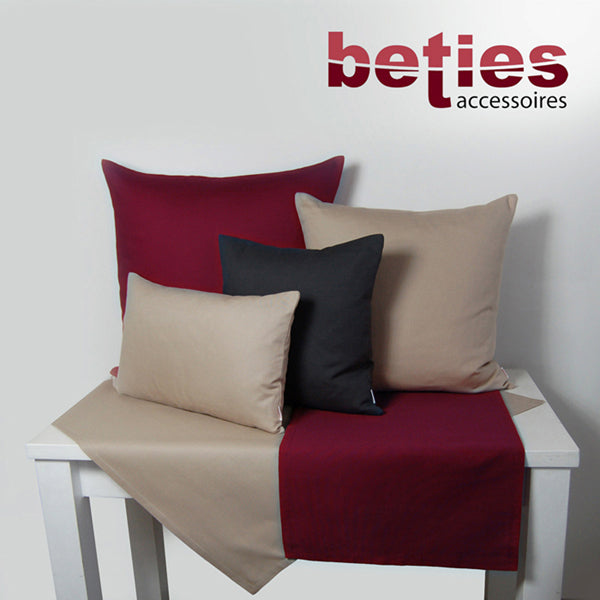 Dunkelgraue und Petrol-Farbene Tischwaesche auf einem weissen Tisch. Darauf stehen vier Kissen mit einfarbigen Kissenbezuegen in den Farben Petrol, Dunkelgrau und Hellgrau.