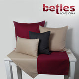 Dunkelgraue und Petrol-Farbene Tischwaesche auf einem weissen Tisch. Darauf stehen vier Kissen mit einfarbigen Kissenbezuegen in den Farben Petrol, Dunkelgrau und Hellgrau.