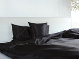 Schwarze Glanz Satin Bettwaesche in einem hellen Bett.
