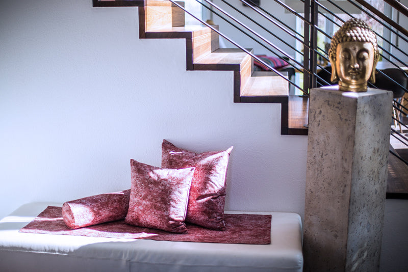 mehrere Kissen auf einer Bank im Hintergrund eine Treppe und eine Buddha Figur