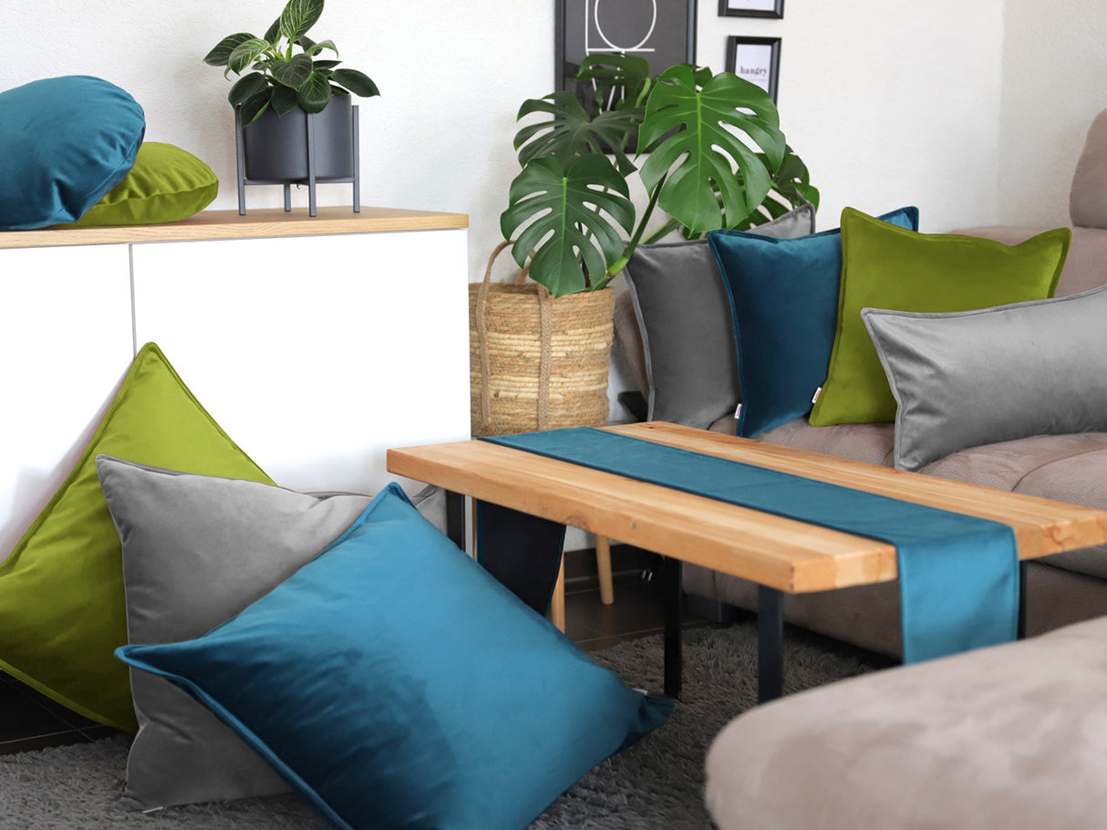 Mai-gruene, petrol-farbene und graue Samt Kissenbezuege und ein petrol-farbenes Samt Tischband sind in einem Wohnzimmer dekoriert.