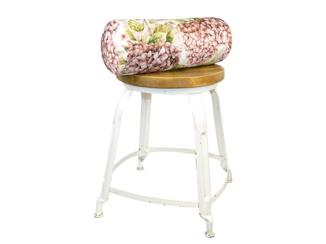Auf einem Hocker liegt ein weisser Bezug für Nackenrollen im Landhausstil, bedruckt mit rosa/pinken Hortensien-Blueten.