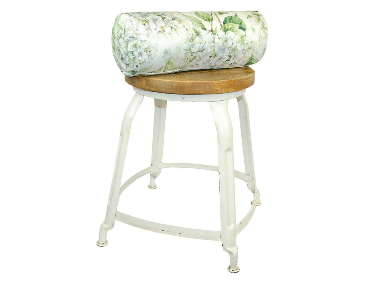 Auf einem Hocker liegt ein weisser Bezug für Nackenrollen im Landhausstil, bedruckt mit rosa/pinken Hortensien-Blueten.