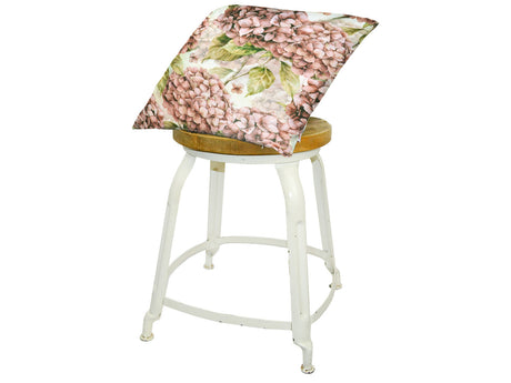 Auf einem Hocker liegt ein quadratischer Kissenbezug im Landhausstil, bedruckt mit rosa/pinken Hortensien-Blueten.