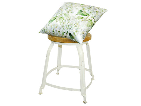 Auf einem Hocker liegt ein quadratischer Kissenbezug im Landhausstil, bedruckt mit weissen Hortensien-Blueten.