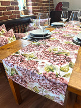 Ein Tischlaeufer bedruckt mit rosa/pinken Hortensien auf einem Holztisch.