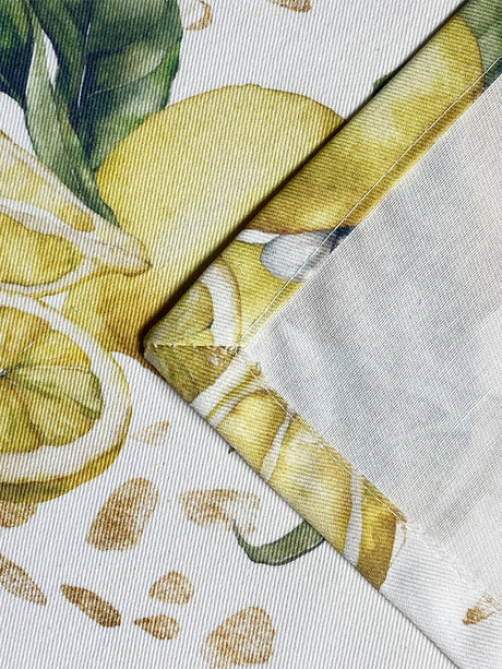 Detailaufnahme einer Ecknaht eines hellbeigen Tischläufers mit Zitronenmuster und goldenen Akzenten.