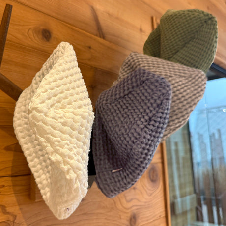 In einer Sauna haengen an einer Holzwand an einem Hirschgeweih vier Waffelpique-Sauna-Beanie aus Baumwoll- Leinenmix in den Farben Gletscher-weiss, Fjord-blau, Nebel-grau und Salbei-gruen.