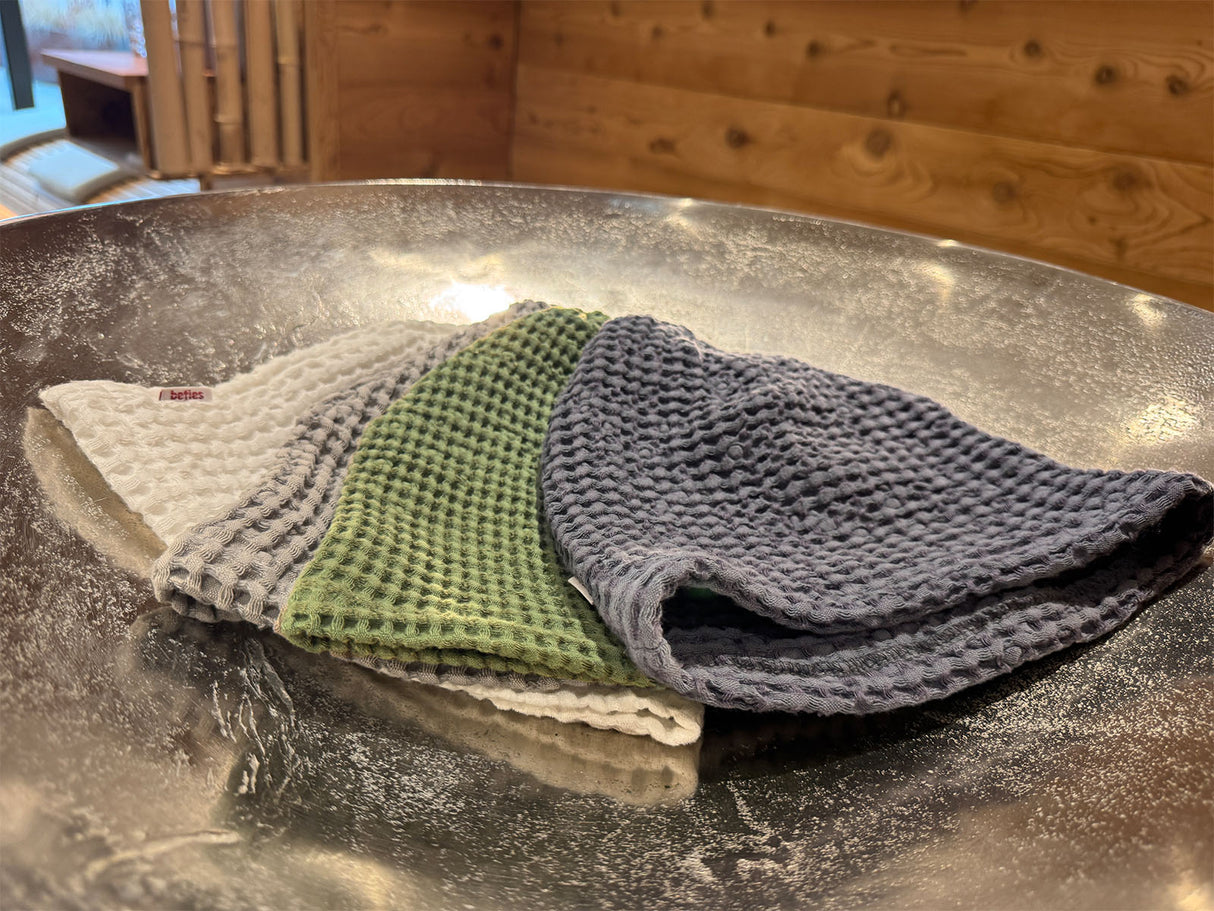 In einer silbernen Schale liegen vier Waffelpique-Sauna-Beanies aus Baumwoll- Leinenmix in den Farben Gletscher-weiss, Fjord-blau, Nebel-grau und Salbei-gruen.