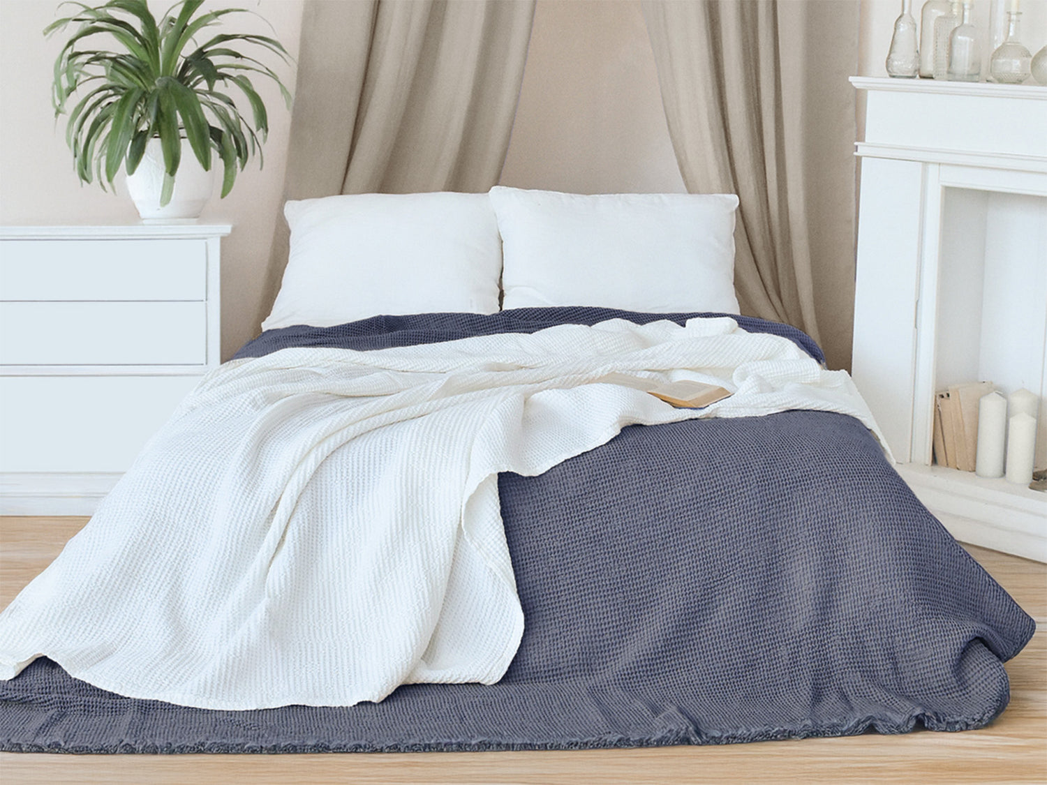 In einem Schlafzimmer liegt eine Gletscher-weisse und eine Fjord-blaue Tagesdecke aus der beties "PUR.NATURE" Serie auf einem Bett ausgebreitet.