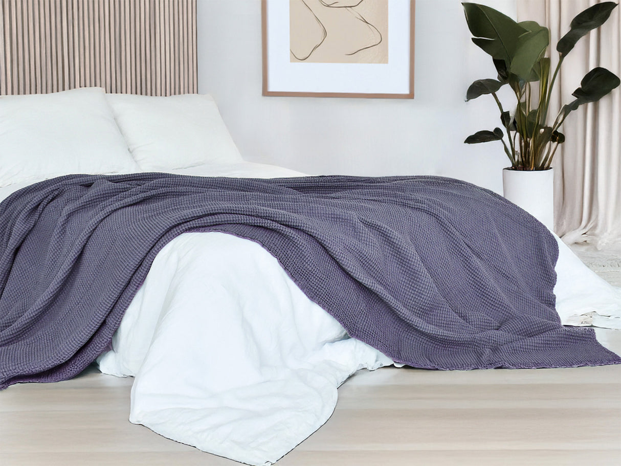 In einem Schlafzimmer liegt eine Fjord-blaue Tagesdecke aus der beties "PUR.NATURE" Serie auf einem Bett ausgebreitet.