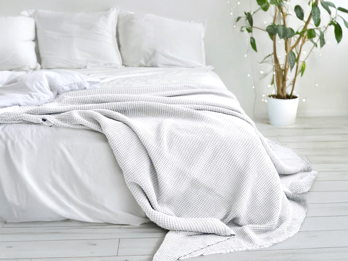 In einem Schlafzimmer liegt eine Gletscher-weisse und eine Nebel-graue Tagesdecke aus der beties "PUR.NATURE" Serie auf einem Bett ausgebreitet.