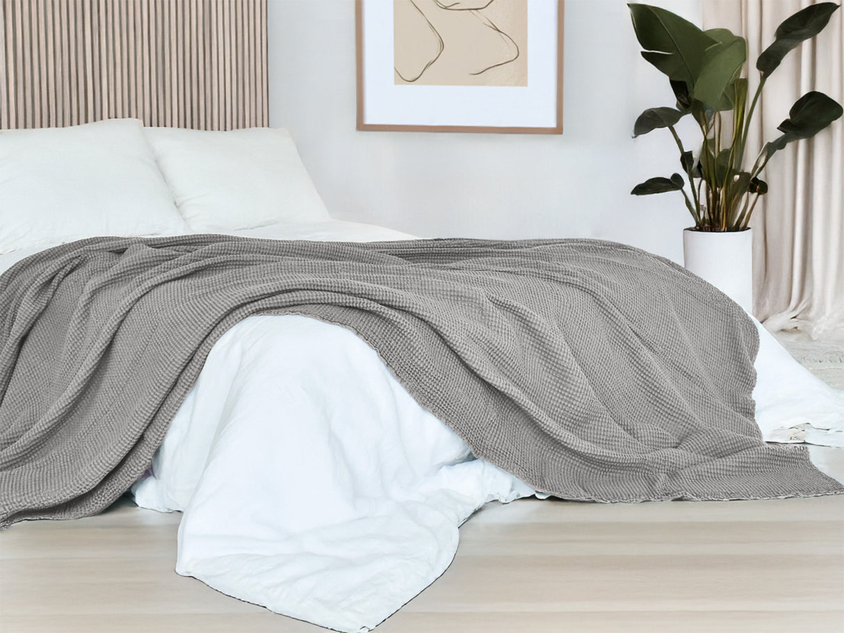 In einem Schlafzimmer liegt eine Nebel-graue Tagesdecke aus der beties "PUR.NATURE" Serie auf einem Bett ausgebreitet.