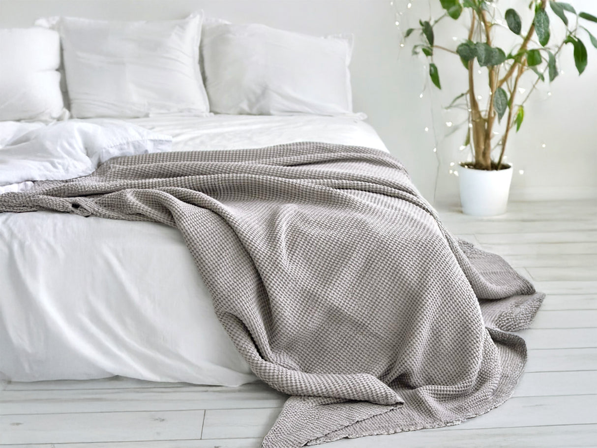 In einem Schlafzimmer liegt eine Nebel-graue Tagesdecke aus der beties "PUR.NATURE" Serie auf einem Bett ausgebreitet.