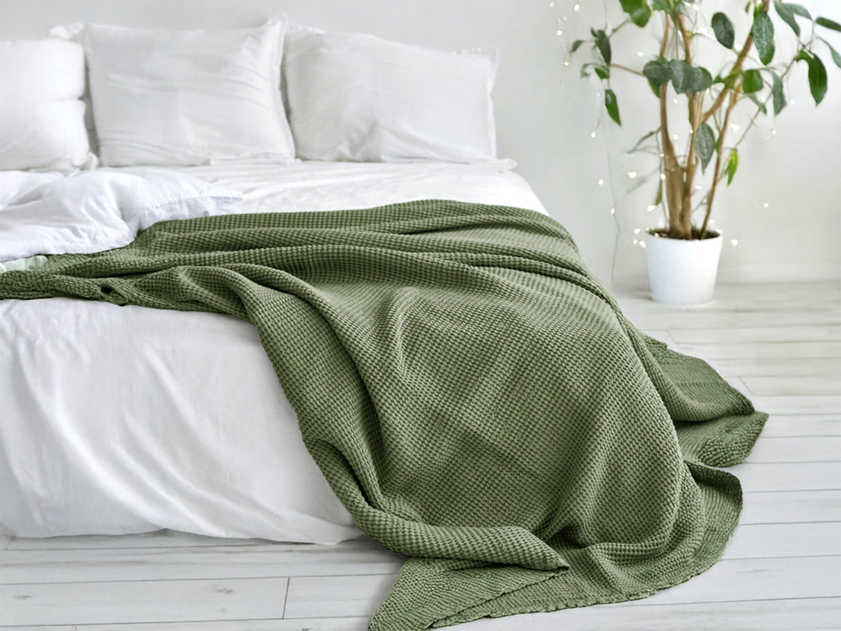 In einem Schlafzimmer liegt eine Salbei-gruene Tagesdecke aus der beties "PUR.NATURE" Serie auf einem Bett ausgebreitet.