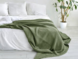 In einem Schlafzimmer liegt eine Salbei-gruene Tagesdecke aus der beties "PUR.NATURE" Serie auf einem Bett ausgebreitet.