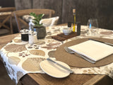 Ein eingedeckter Holztisch mit einer, mit taupefarbenen und braunen Blaettern, Zweigen und Voegeln bedruckten, Mitteldecke.