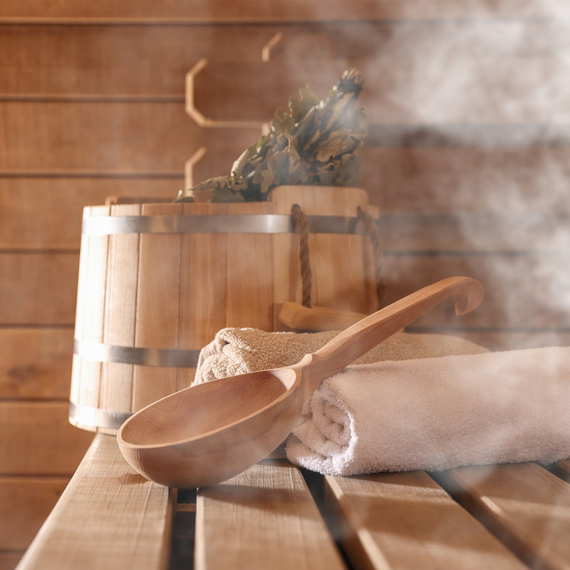 Sauna mit hölzernem Saunaeimer, Holzschöpfkelle, Handtücher und aufsteigendem Dampf.